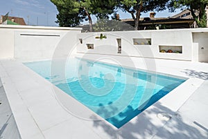 A white marble pool filled with inviting chlorinated water, a garden with a lawn and trees and niches with flower pots on one wall