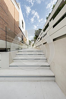 White marble stairs of a corridor of a detached house with palm trees, glass railing and brick and marble facade