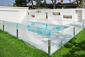 A white marble swimming pool with a glass railing, a lawned garden and flower pot niches in one wall photo