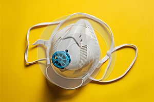 White mask with blue valve on yellow background, with head strap and rubber valve