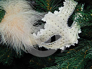 A white mask with a feather in the Christmas tree as a background.