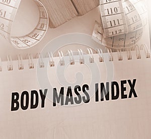 A white measuring tape and copybook with BMI body mass index words. Healthcare healthy living concept
