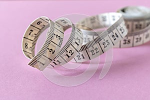 White measuring tape on a pink background. Close-up