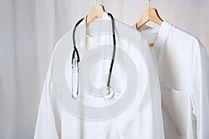 White medical doctor or physician lab coats with stethoscope hanging on clothes hangers, copy space