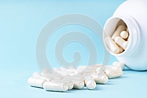White medical pills and capsules spilling out of bottle. Medication in white container on blue background