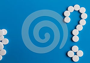 White medical pills question mark on blue background, conceptual image. Medications for the treatment of patients