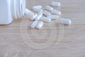 White medical pills spilling out of a drug bottle on a wooden backgrounds