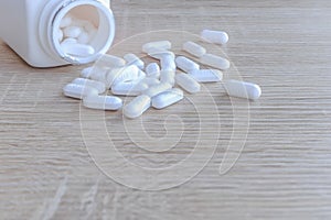 White medical pills spilling out of a drug bottle on a wooden backgrounds