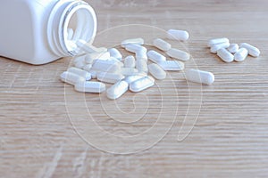 White medical pills spilling out of a drug bottle on a wooden backgrounds