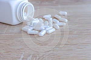 White medical pills spilling out of a drug bottle on a wooden backgrounds