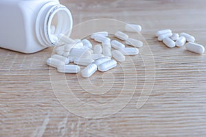 White medical pills spilling out of a drug bottle on a wooden backgrounds