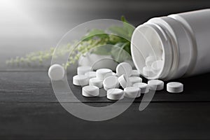 White medical pills and tablets spilling out of a drug bottle. top view with copy space. On Black wood Background. Natural herbs,