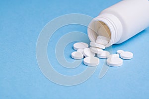 White medical tablets and pills spilled out of a medicine bottle. Macro top down view