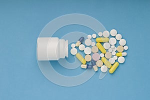 White medicine bottle and medicine pills, tablets and capsules on blue background