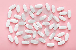 White medicine capsules on pink background.