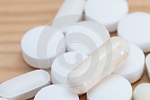 White medicine capsules and white tablets on a wooden background