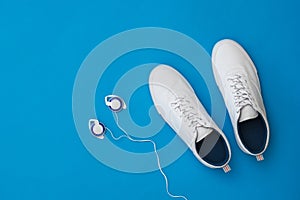 White men`s sneakers and over-ear headphones on a blue background. Sports style. Flat lay.