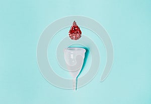 White menstrual cup  with a drop of blood on a blue background