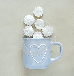 The white merengues in a cup on beige background, flat lay, top view. A blue cup with heart