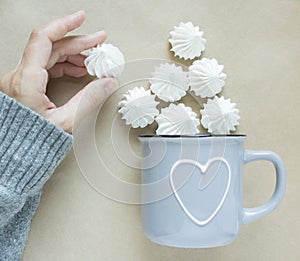 The white merengues in a cup on beige background top view. A cup with heart in women hand