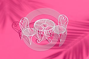 White metal chair and table on bright pink background. Creative trendy layout with sunshine and hard shadow. Cafe, restaurant,