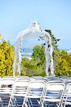 White metal folding chairs lined up for outdoor wedding with arbor and view