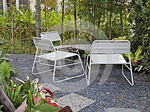 White metal outdoor furnitire in the tropocal garden surround with plants on the gravel floor