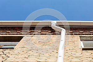 White metal pipe from the drain on the wall of a brick building. Water drainage from the roof. Drain on the roof of the