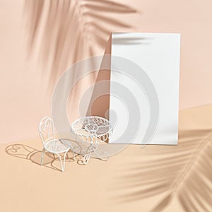 White metal table and chair on beige background. Minimal creative layout with sunshine and hard shadow. Palm leaves shadow and