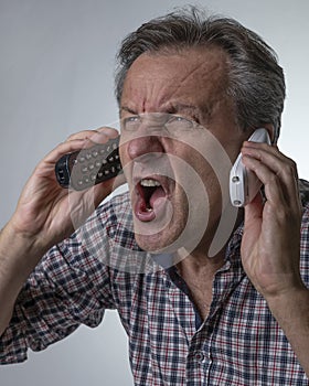 A white man yells while holding two cordless phones, with an expression of great stress