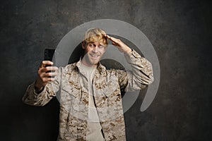 White military man saluting while taking selfie on cellphone