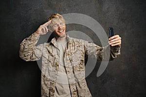 White military man saluting while taking selfie on cellphone