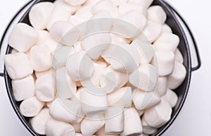 White mini puffy marshmallows ia a black bowl on white background with copy spase. Top view, close-up.