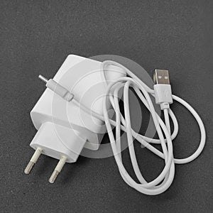White mobile phone charging adapter with white USB type cable on black surface