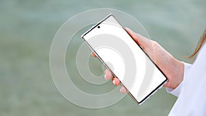 White mockup smartphone in female hands. Woman use mobile phone to search in internet, app outside. Closeup female hands with