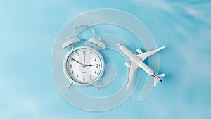 White model airplane and alarm clock on blue background. Travel concept