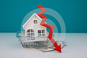 White model of house in basket with down arrow. Falling of real estate market prices