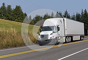 White big rig semi truck transporting dry van semi trailer on th