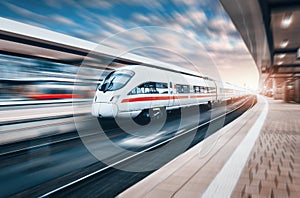 White modern high speed train in motion on railway station at su
