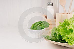 White modern kitchen decor with beige natural wooden dish, utensils, fresh green salad on wood background.