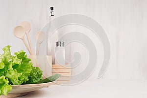 White modern kitchen decor with beige natural wooden dish, utensils, fresh green salad on wood background.