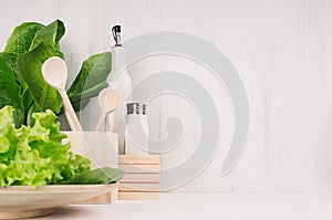 White modern kitchen decor with beige natural wooden dish, utensils, fresh green salad on wood background.