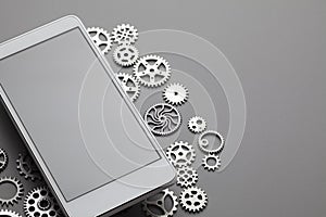 White modern mobile phone with blank gray screen and small gears on table