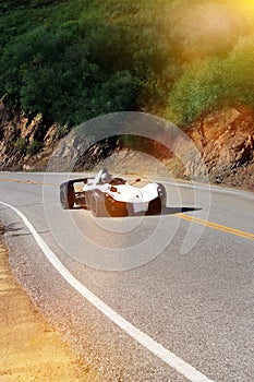 White modern sport car is driving on empty countryside asphalt road at sunset