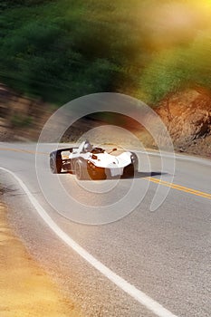 White modern sport car is driving on empty countryside asphalt road at sunset.