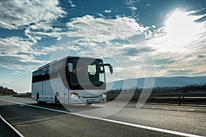 White Modern tourist bus driving through highway on bright sunny sunset