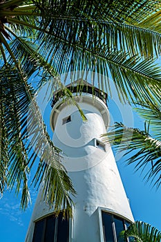 The white monolite structure of the lighthouse rises overover a palms tree. Thailand, Bangok. The massive tower of an