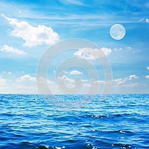 White moon in blue sky with clouds over the sea at daytime