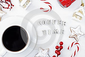 A white mug of black Americano coffee on a white wooden background next to Christmas cookies, a candy cane and New Year`s toys.