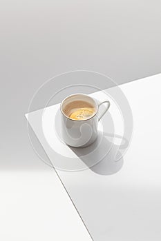 White mug with coffee on a gray background with shadows of leaves. Top view, close-up